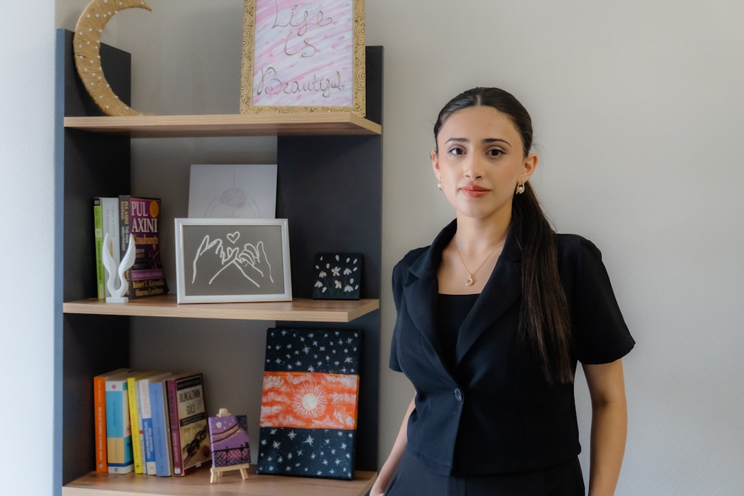 Young woman in black blazer stands by bookshelf