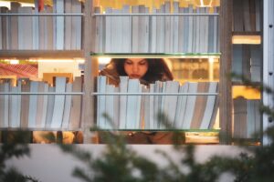 Woman peeking through bookshelves at bookshelf