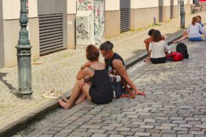 Couple sitting on cobblestone street near building.