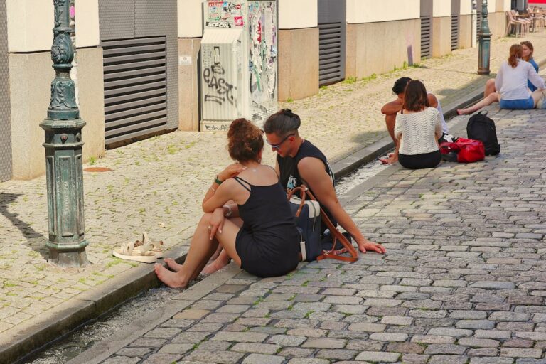 Couple sitting on cobblestone street near building.