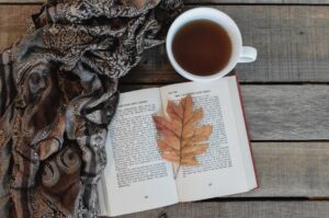 an open book with a leaf on top of it next to a cup of coffee