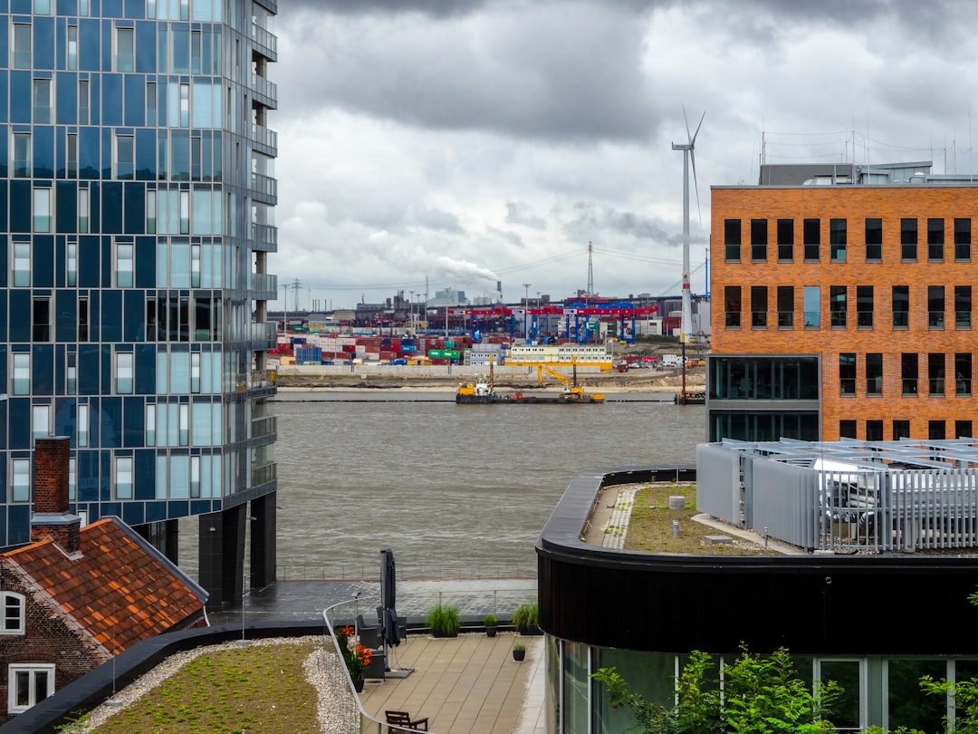 Modern buildings overlook a busy port with cranes and ships.