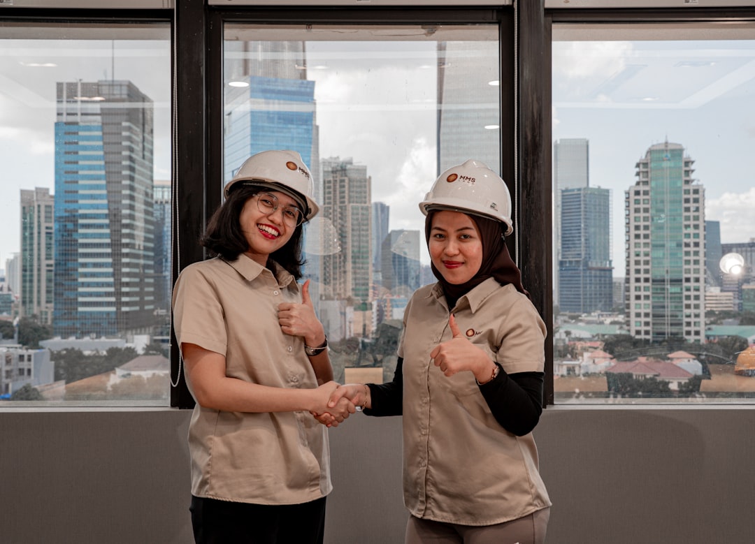 Two women in hard hats shake hands with city skyline.