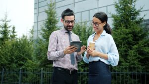 Two colleagues discuss a tablet outside an office building.
