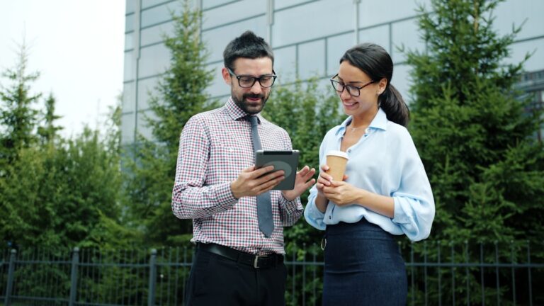 Two colleagues discuss a tablet outside an office building.