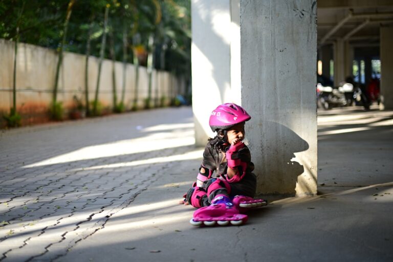 Young girl in pink helmet and roller skates sitting.