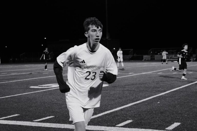 Young male soccer player running on field at night.