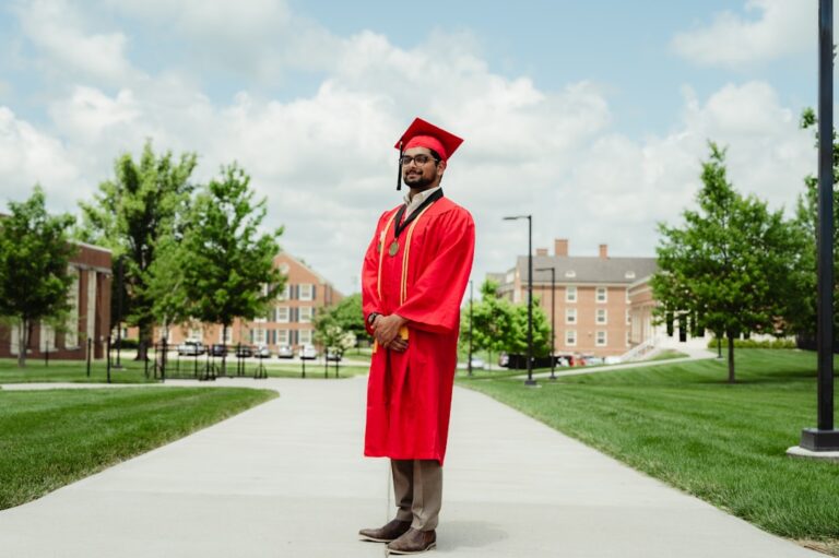 A man in a red graduation gown standing on a sidewalk