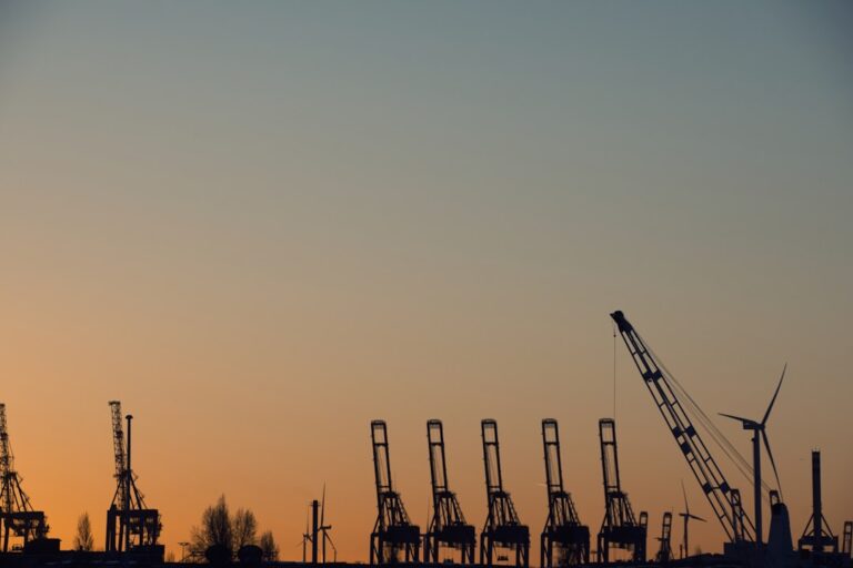Silhouetted industrial cranes against a sunset sky