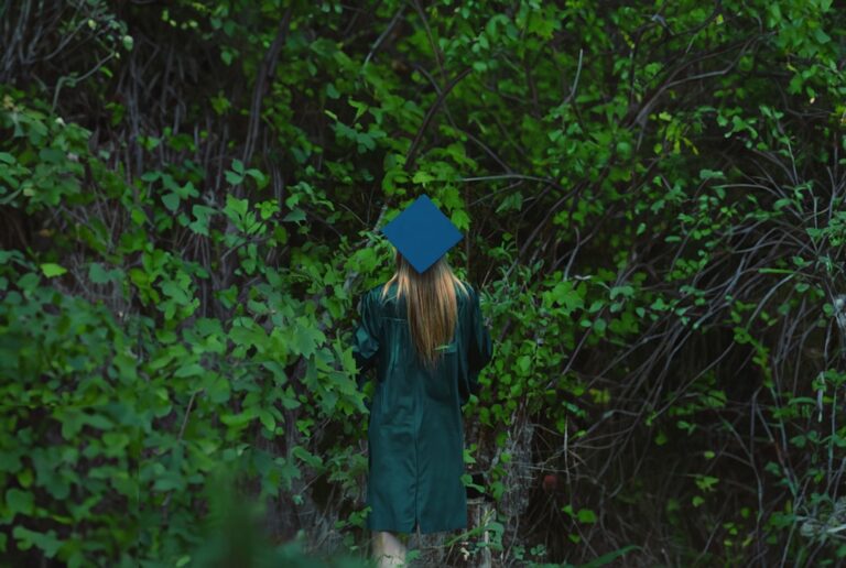 a woman in a graduation gown walks through the woods