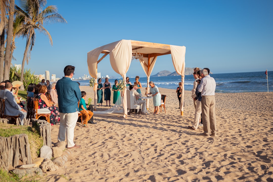Beach wedding ceremony with guests under a canopy.