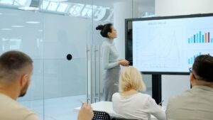 Woman presents charts on a screen to colleagues.