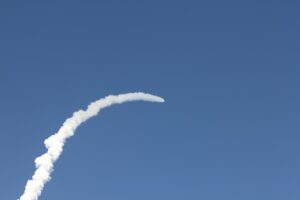A rocket trail arcs across a clear blue sky