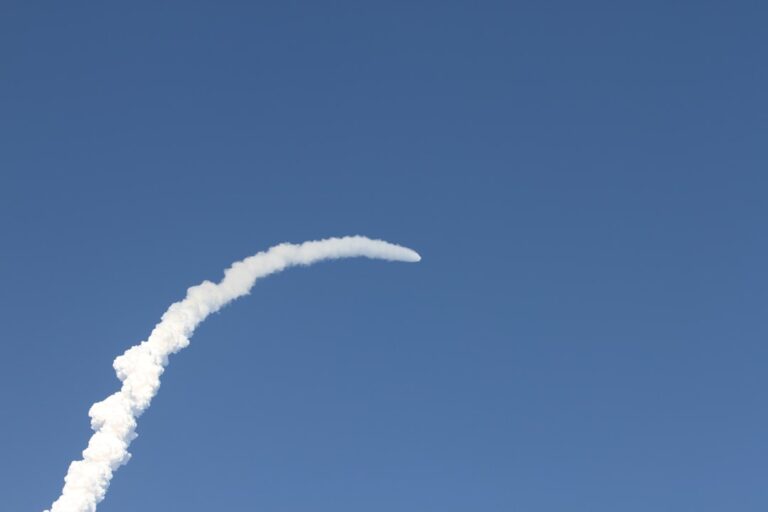 A rocket trail arcs across a clear blue sky