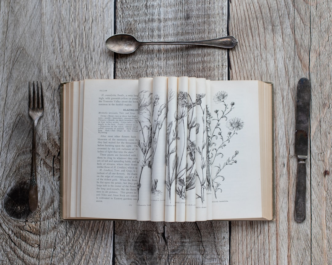 Open book with botanical drawings between cutlery.