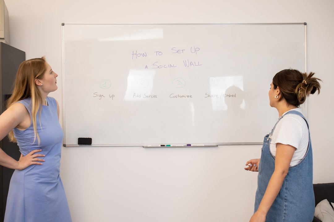 two women standing in front of a white board