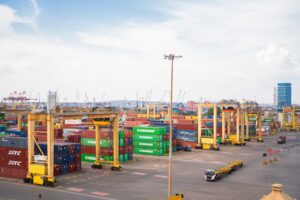 Shipping containers stacked at a busy port with cranes.