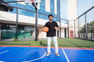 Young man holding basketball on blue court, giving thumbs-up.