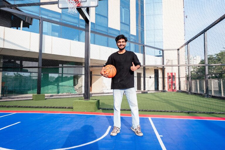 Young man holding basketball on blue court, giving thumbs-up.