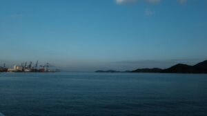 Industrial port with cranes on the left, ocean and hills.