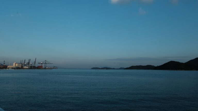 Industrial port with cranes on the left, ocean and hills.