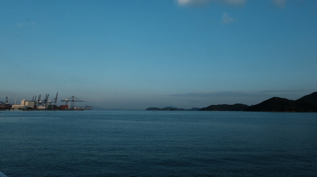 Industrial port with cranes on the left, ocean and hills.