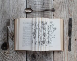 Open book with botanical drawings between cutlery.