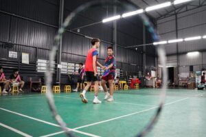 Two men shake hands on an indoor badminton court.