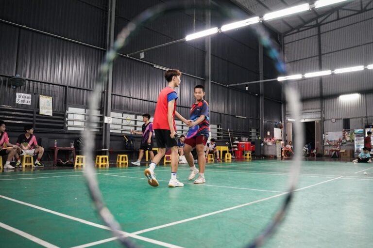 Two men shake hands on an indoor badminton court.