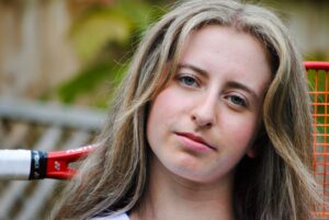 Young woman with long blonde hair and tennis racket.