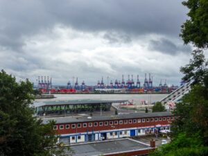 Container cranes at a busy industrial port under cloudy skies