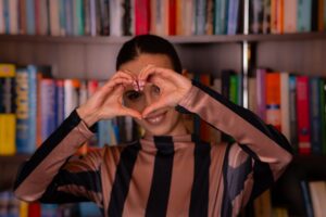 Woman making heart shape with hands in front of bookshelf