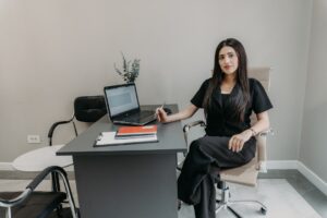 Woman in black sitting at office desk with laptop.