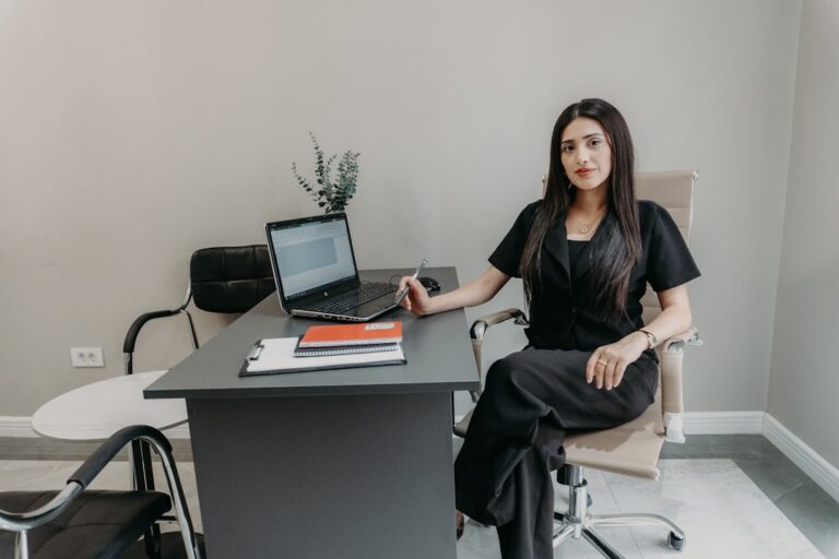 Woman in black sitting at office desk with laptop.