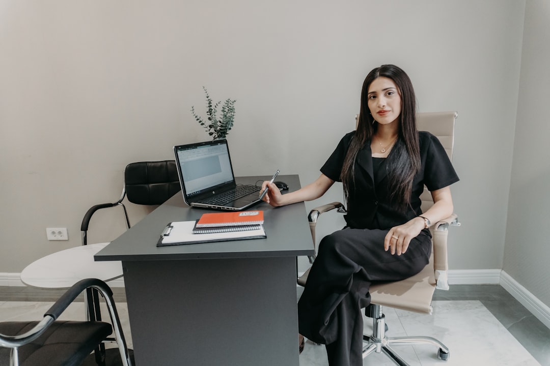Woman in black sitting at office desk with laptop.