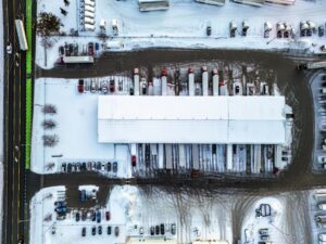 Aerial view of a snowy industrial warehouse with trucks.