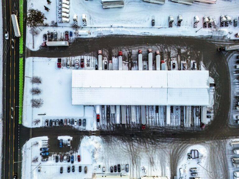 Aerial view of a snowy industrial warehouse with trucks.