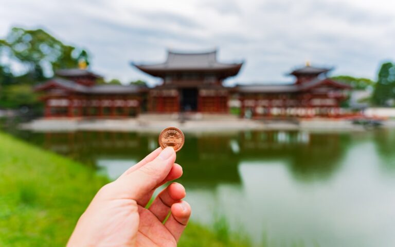 Hand holding a coin in front of a temple.