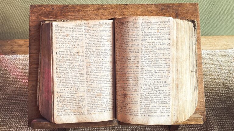 An open, aged book rests on a wooden stand.
