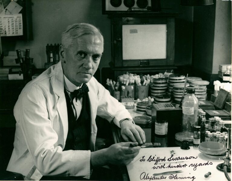 Scientist in lab coat with petri dishes and equipment.