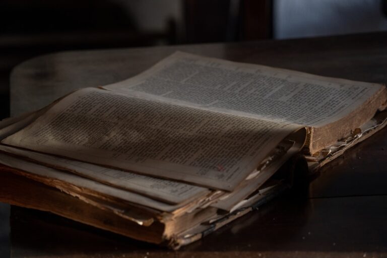 An old, weathered book lies open on a wooden table.