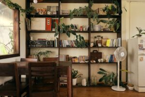 A cozy room with a bookshelf, plants, and dining table.