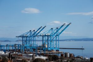 Blue container cranes dominate a port with calm water.
