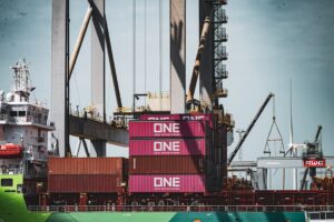 Train with pink containers at a busy shipping port.