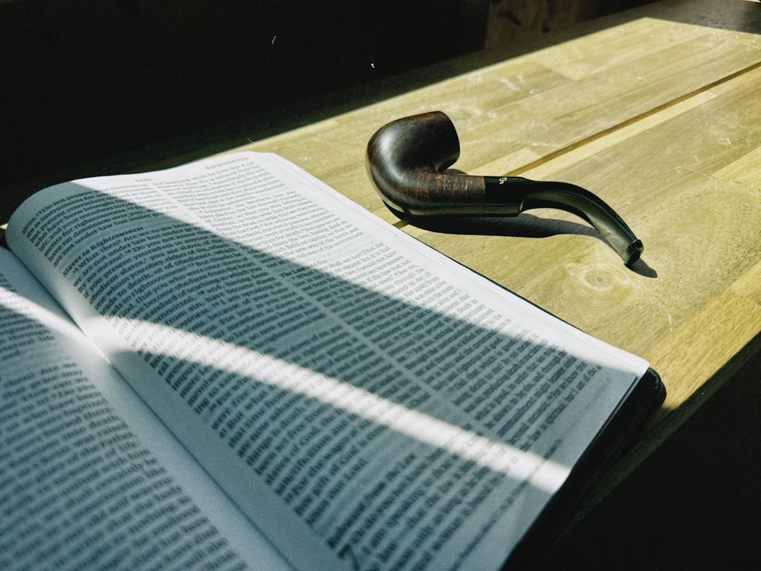 An open book and a pipe on a wooden table.