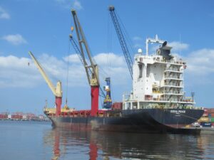 Cargo ship with cranes docked at a busy port.