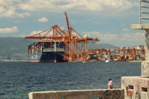 Large cargo ship docked at a busy port with cranes.