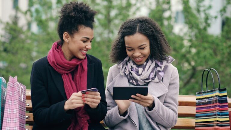 Two women looking at a tablet with shopping bags.