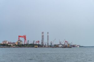 An industrial port with cranes and structures seen across water.