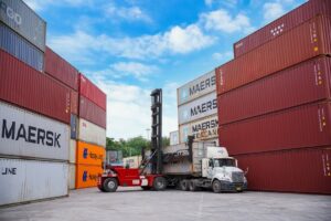 Forklift moving shipping containers at a port.